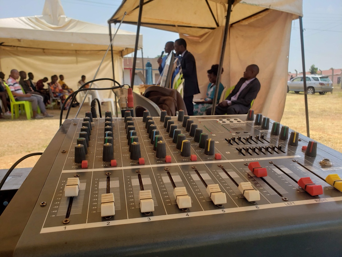 Outdoor crusade in Uganda — sound mixer, tent, pastors and seated congregation