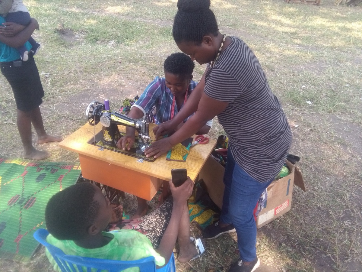 Ugandan women learning to use a sewing machine in an outdoor skills training session